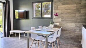 Un moderno comedor con una mesa dispuesta para cuatro personas, un televisor de pantalla plana en la pared y una ventana con vistas a zonas verdes.