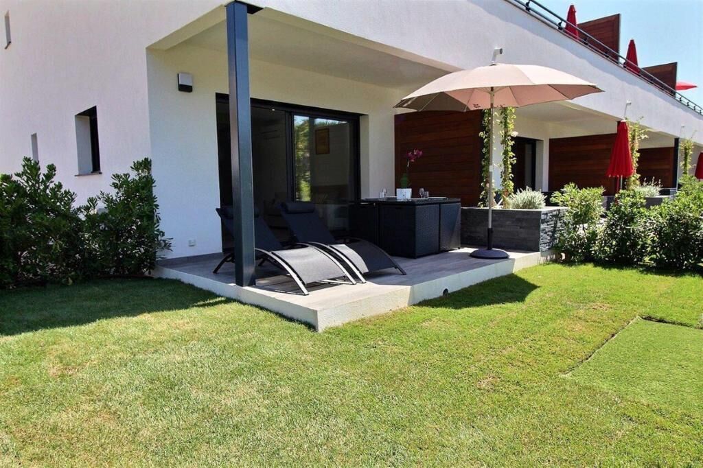 Un patio moderno al aire libre con una zona de estar, una mesa y un gran paraguas.
