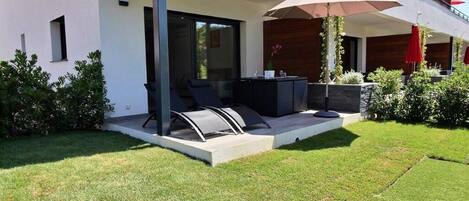 Un patio moderno al aire libre con una zona de estar, una mesa y un gran paraguas.