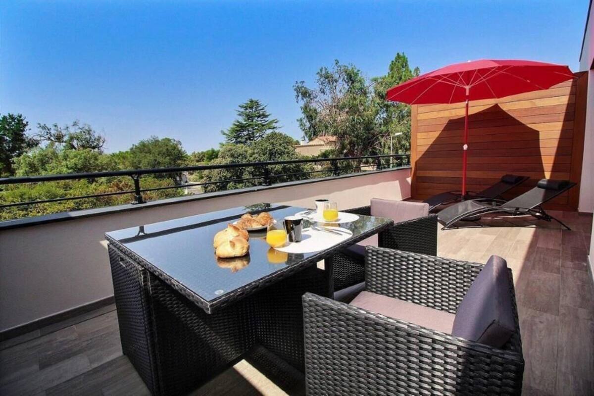 A balcony with a table set for breakfast, wicker furniture, and a red umbrella.