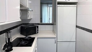 A compact kitchen with white cabinets, a black microwave, a stove, and a refrigerator. - Cozy apartment in the Barrio de las Letras in Madrid (Madrid)
