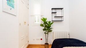 A bedroom with a bed, a radiator, a wall-mounted shelf, a window, and a potted plant. - Cozy apartment in the Barrio de las Letras in Madrid (Madrid)