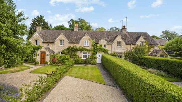Une grande maison en pierre dotée de plusieurs toits à pignons, d’une allée gravillonnée et de jardins bien entretenus.