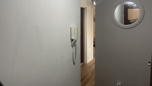 En gang med hvid væg, en dør med spejl og en vægtelefon.