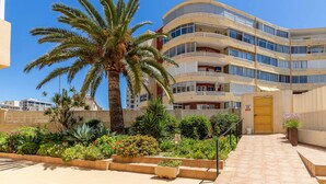 Ein mehrstöckiges Hotel mit Balkonen, einer Palme und einem gepflegten Garten mit verschiedenen Pflanzen und Blumen.