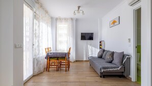 Ein Zimmer mit Esstisch, Stühlen, einer Couch, einem Fernseher und einer Klimaanlage.