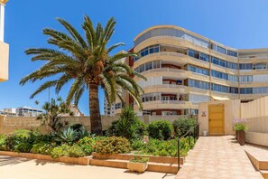 A multi-story hotel with balconies, a palm tree, and a well-maintained garden with various plants and flowers. - Inftour President 3 Apartamento (Calp)