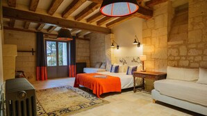 Un dormitorio acogedor con una cama grande, una cama más pequeña, un sofá blanco, suelo de madera, paredes de piedra y un amplio ventanal.
