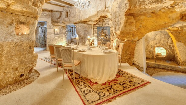 Comedor con paredes de piedra, una araña y una mesa dispuesta para cuatro.