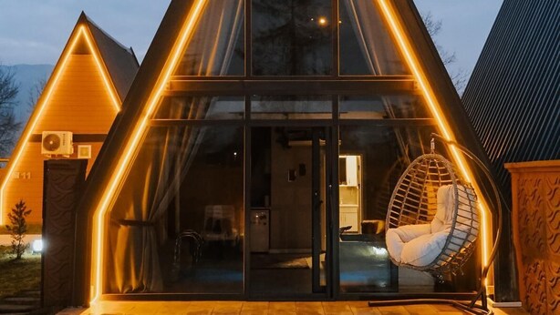Ein modernes Haus mit einem dreieckigen Dach, einem Glastür-Eingang und einem Pool davor.