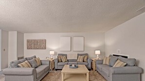 A living room with two grey sofas, a coffee table, and two side tables with lamps. There are two framed pictures on the wall and a decorative piece above the coffee table.