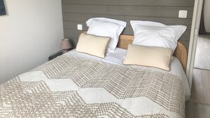 A neatly made bed with a patterned bedspread, a headboard with a horizontal panel design, and a bedside lamp. - House facing the sea 3* classification (Langrune-sur-Mer)