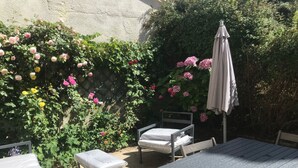 An outdoor patio with a table and chairs, surrounded by lush greenery and flowering plants. - House facing the sea 3* classification (Langrune-sur-Mer)