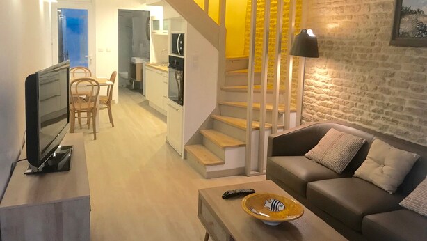 A modern living room with a sofa, a TV, and a remote control on a coffee table. A staircase with yellow accents leads to an upper level. - House facing the sea 3* classification (Langrune-sur-Mer)