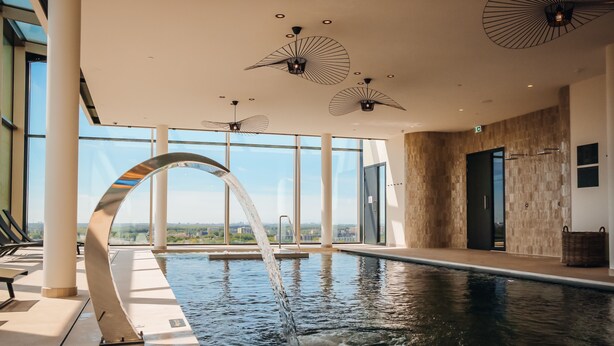 En inomhuspool med klart vatten, en böjd utsiktsplattform och moderna takfläktar.