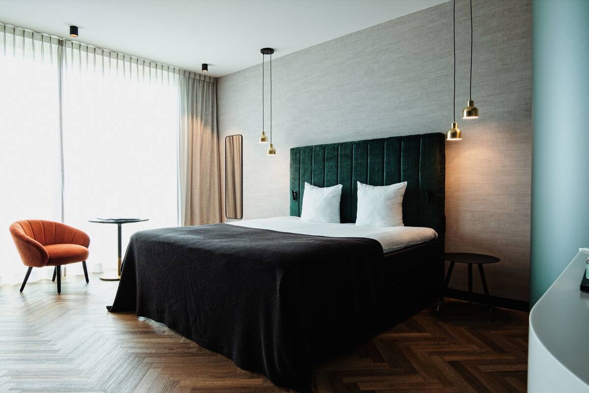 Une chambre d’hôtel moderne, dotée d’un grand lit, d’une chaise, d’une petite table et offrant une vue sur l’extérieur.