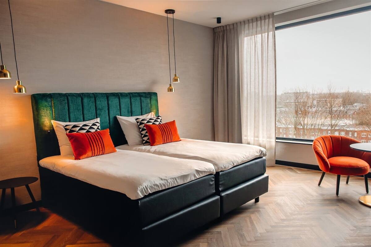 Une chambre d’hôtel moderne avec un grand lit, deux tables de chevet, une chaise et une vue sur la ville.