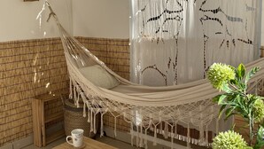 Una hamaca en una habitación con un muro tejido, una mesa de madera y una lámpara colgante.