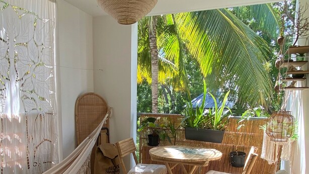 Un espacio al aire libre acogedor con una hamaca, sillas de mimbre y una mesa.