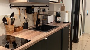 Una cocina moderna con encimera negra, estufa integrada y microondas. Hay utensilios de madera y una cafetera en la encimera.