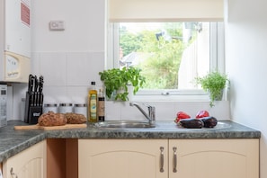 A kitchen with a granite countertop, a stainless steel sink, and a window with a view of greenery outside.