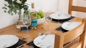 Una mesa de comedor con platos, cubiertos, copas de vino, una botella y un bol de manzanas verdes.