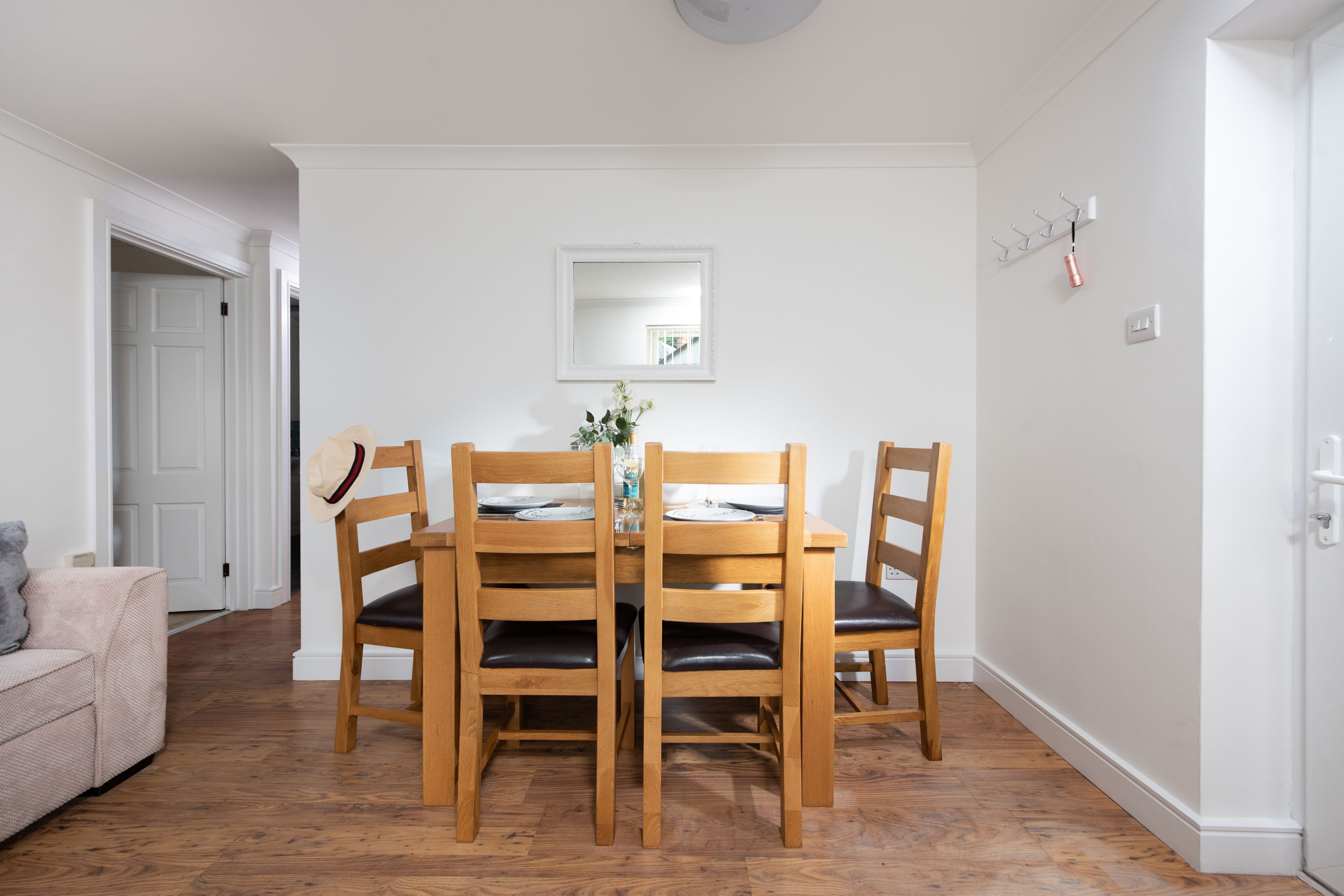 Ein Essbereich mit einem Holztisch und Stühlen, einer kleinen Vase mit Blumen und einem Spiegel an der Wand.