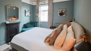 A bedroom with a large bed, a fireplace, a window with curtains, and a wall-mounted mirror. - Host & Stay | The Railman's House (York)