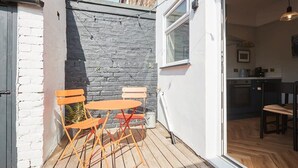 A small patio with a wooden table and chairs, a stone wall, and a view into a kitchen area. - Host & Stay | The Railman's House (York)