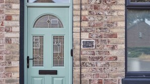 A light blue door with a small window and a mail slot, set in a brick wall with a window above it. - Host & Stay | The Railman's House (York)