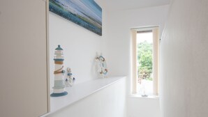 A white interior with a painting of a seascape, a lighthouse, and a small sailboat on a shelf. - Kerensa is a cosy and detached barn conversion located in the lovely seaside village of Portreath (Portreath)