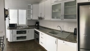 A modern kitchen with white cabinets, a stainless steel refrigerator, a built-in oven, and a granite countertop.