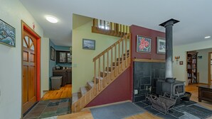 Un salon avec une cheminée, un escalier en bois et un coin cuisine.