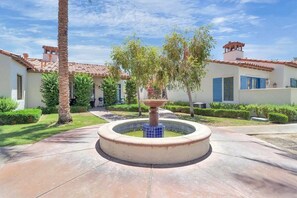 A courtyard with a fountain, palm trees, and a building with a tiled roof.