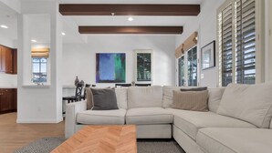 Een moderne woonkamer met een hoekbank, een salontafel met een herringbone-patroon en een groot abstract schilderij aan de muur.