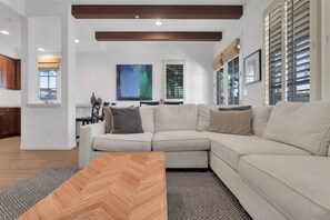 A modern living room with a sectional sofa, a herringbone-patterned coffee table, and a large abstract painting on the wall.