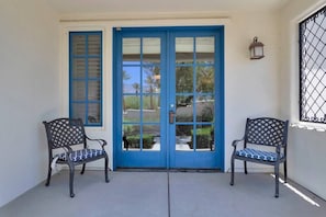 A set of blue doors with a window on the left, two benches with patterned cushions, and a wall-mounted lantern. - Mountain-view 3BR condo in Legacy Villas with pool, fireplace, and balcony. (La Quinta)