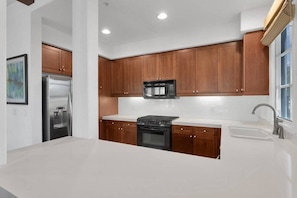 A modern kitchen with wooden cabinets, a stainless steel refrigerator, a black microwave, and a built-in oven. - Mountain-view 3BR condo in Legacy Villas with pool, fireplace, and balcony. (La Quinta)