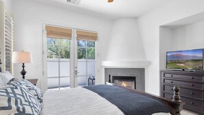 Een slaapkamer met een bed, een open haard, een televisie en een raam met zonwering.