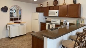Una cocina con una isla central, armarios de madera, microondas, estufa y refrigerador.
