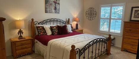 Een slaapkamer met een houten bed, twee nachtkastjes, een wanddecoratie en een plafondventilator, inclusief een raam met jaloezieën.