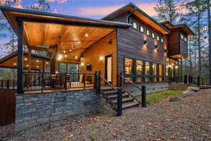 A modern log cabin with a covered porch, stone foundation, and multiple windows.