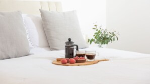 A neatly made bed with pillows, a coffee maker, a tray with toast and raspberries, and a cup of coffee.