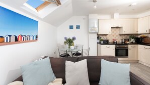 A modern apartment with a dining area, kitchen, and a living room with a sofa and cushions.