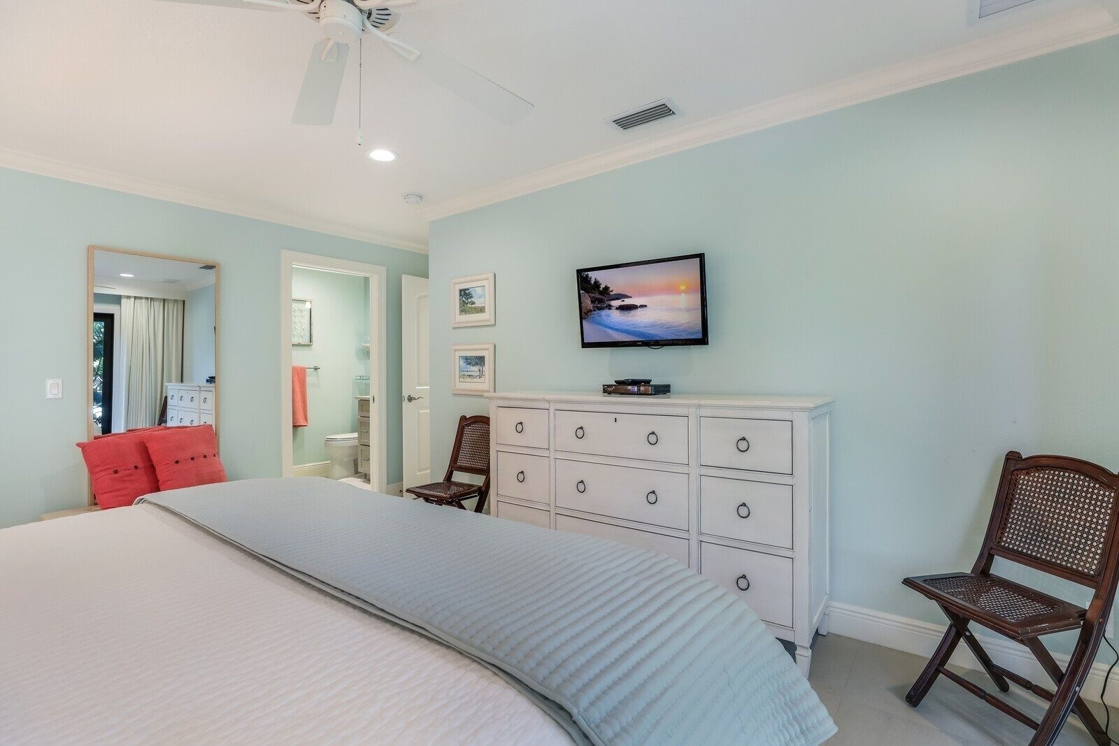 Un dormitorio con cama, cómoda, silla, televisión y ventilador de techo.