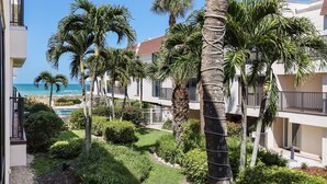 A beachfront hotel with multiple-story buildings, palm trees, and a view of the ocean. - Waters Edge 104s 2 Bedroom Condo by RedAwning (Holmes Beach)
