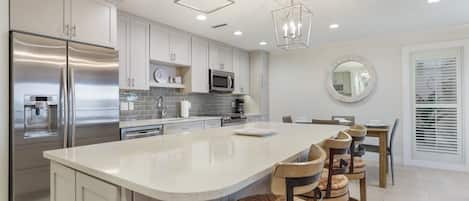A modern kitchen with a large island, stainless steel appliances, and a dining area with wooden chairs.