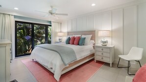 A modern bedroom with a large bed, a ceiling fan, a nightstand with a lamp, and a chair. - Waters Edge 104s 2 Bedroom Condo by RedAwning (Holmes Beach)