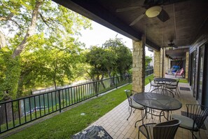 A covered patio with outdoor seating, a view of a river, and a stone wall. - River Bend Cw C109 3 Bedroom Condo by RedAwning (New Braunfels)
