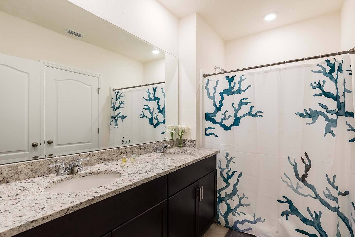A bathroom with a white sink, dark cabinets, and a shower curtain with blue tree-like patterns.